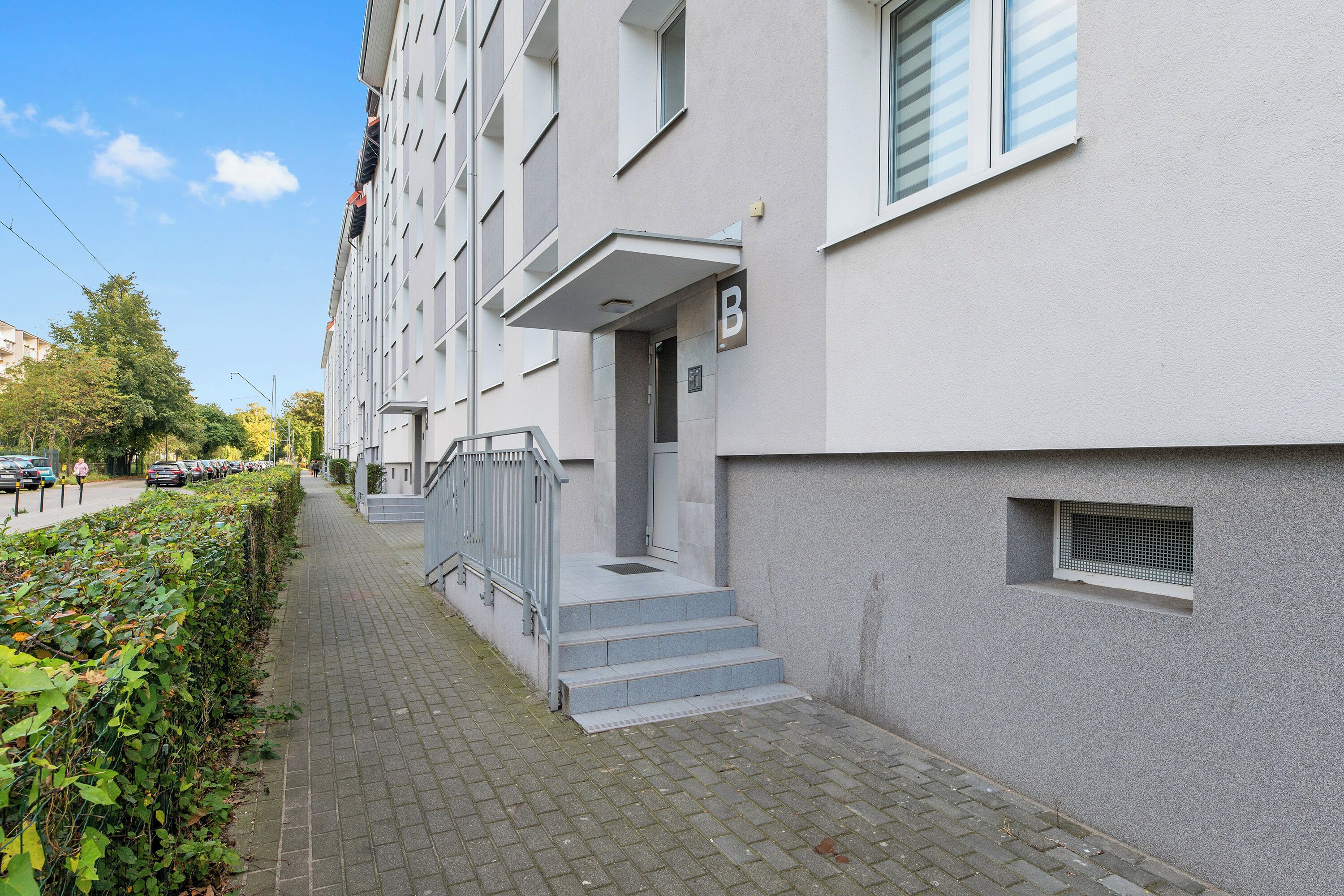 Een modern appartementencomplex met een grijze gevel, een duidelijke ingang met treden en een klein raam met een metalen traliewerk.