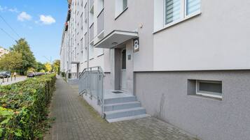 Een modern appartementencomplex met een grijze gevel, een duidelijke ingang met treden en een klein raam met een metalen traliewerk.