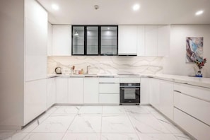 A modern kitchen with white cabinetry, a marble backsplash, and a built-in oven.