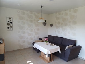 Un salon comprenant un canapé, une petite table recouverte d’une nappe blanche, un luminaire suspendu et des œuvres d’art décoratives accrochées au mur.