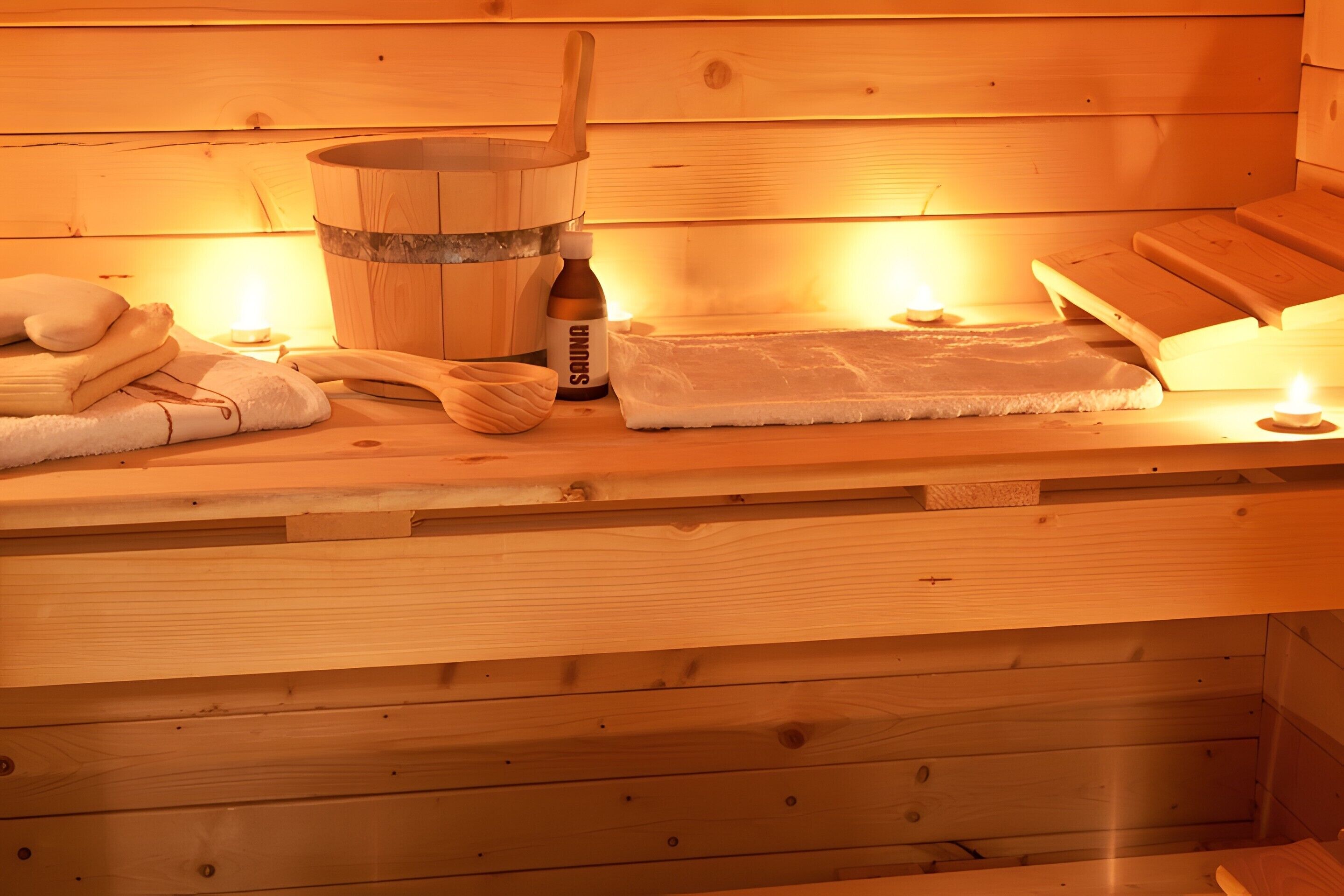 Un sauna en bois, avec des serviettes, un seau en bois et une bouteille portant l’étiquette « SAUNA ».