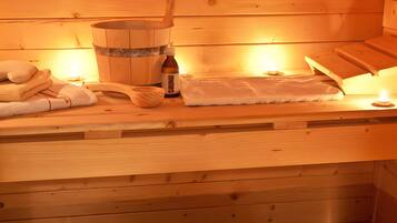 Un sauna en bois, avec des serviettes, un seau en bois et une bouteille portant l’étiquette « SAUNA ».
