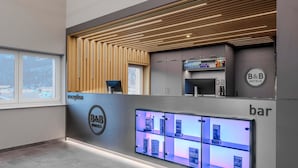 A B&B hotel reception area with a bar, a digital menu display, and a view of the outside. - B&B Hotel Mittenwald (Mittenwald)
