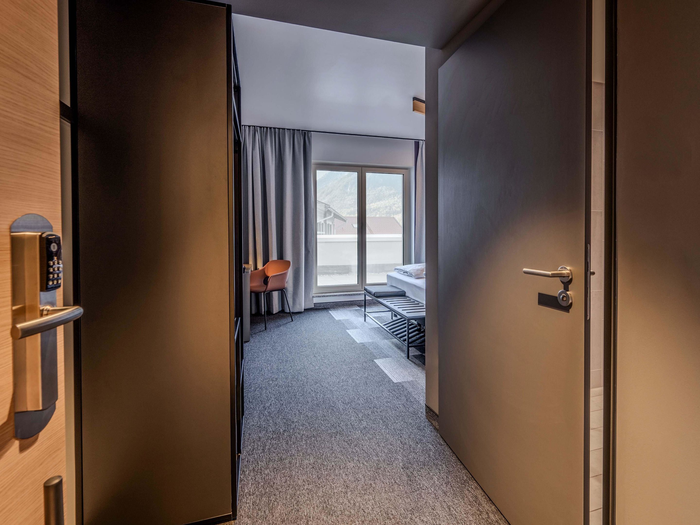Una habitación de hotel con puerta corrediza que da a un balcón, una cama, un escritorio y una silla.