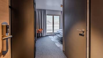 A hotel room with a sliding door leading to a balcony, a bed, a desk, and a chair.