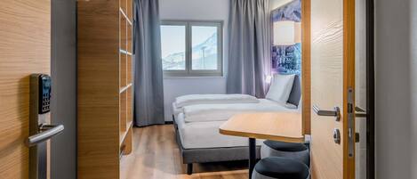 Una habitación de hotel moderna con una cama, una mesita, una silla y un armario.
