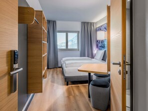 Una habitación de hotel moderna con una cama, una mesita, una silla y un armario.
