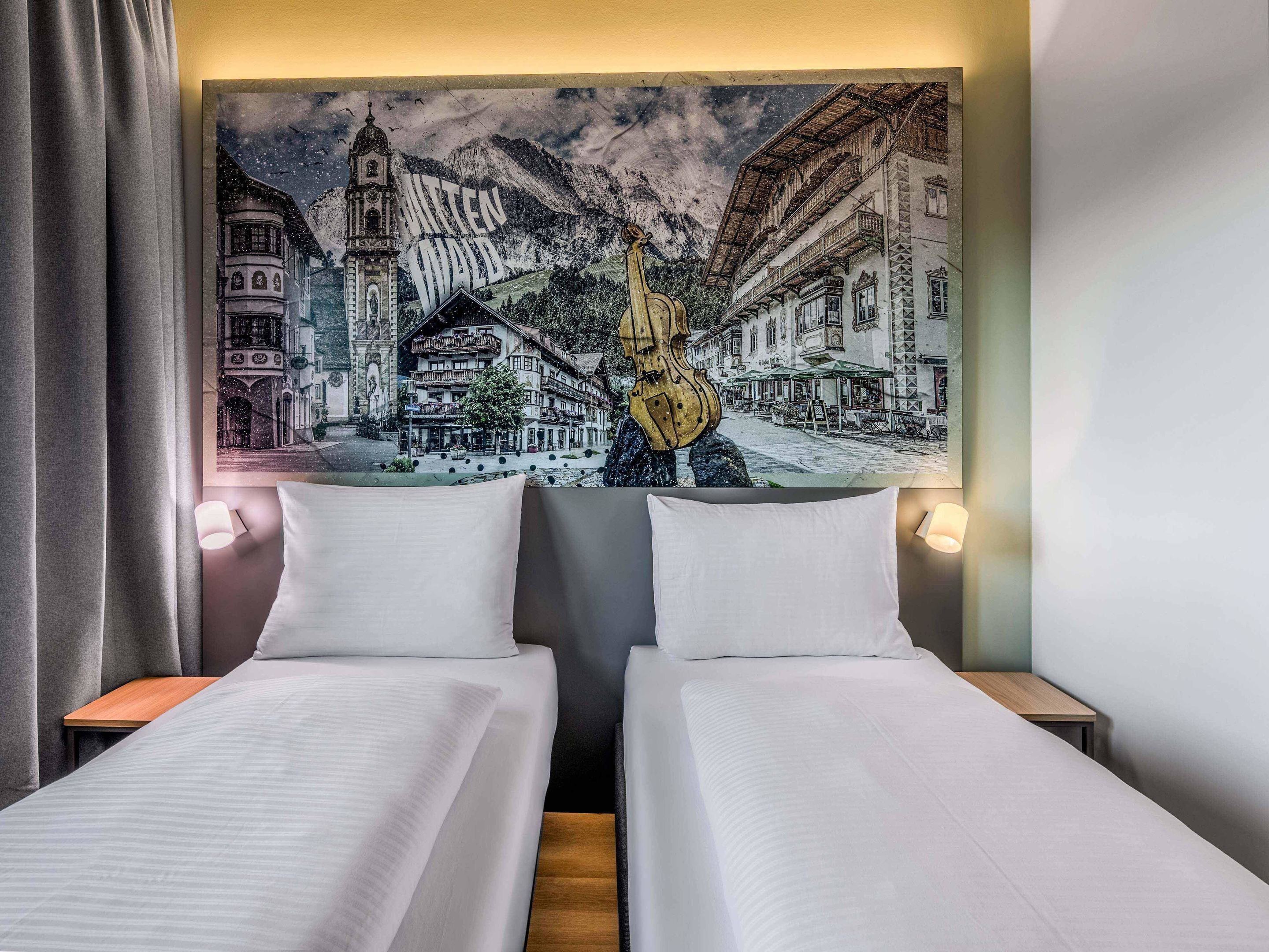 A hotel room with two beds, a large tapestry depicting a mountain scene, and a wooden nightstand.