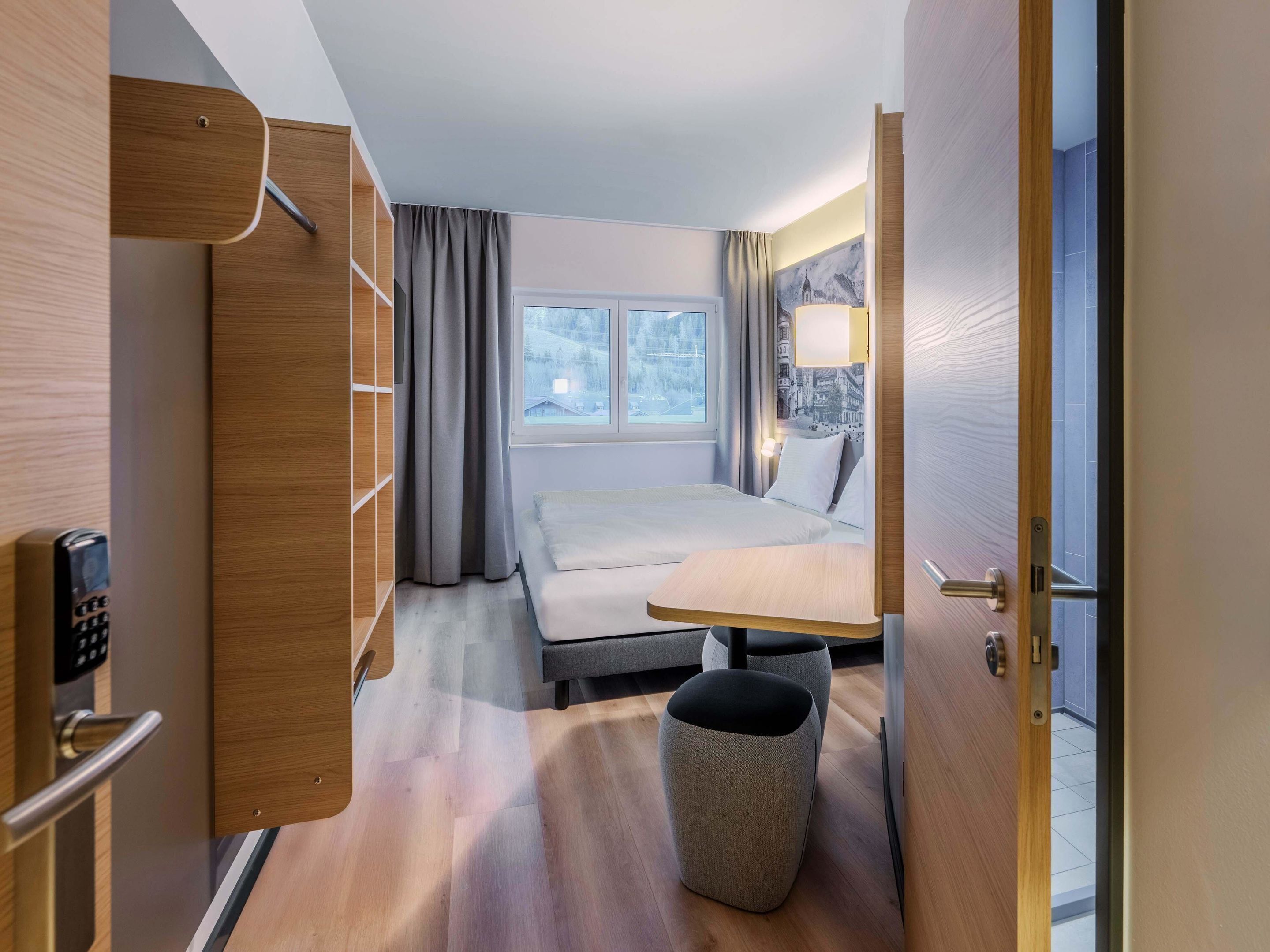A modern hotel room with a bed, bedside table, and a view of a snowy landscape through the window.