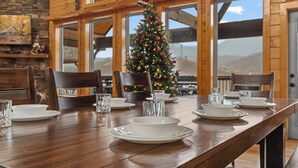 Ein Esstisch für vier Personen, gedeckt mit weißen Tellern und klarem Glas, mit einem Weihnachtsbaum im Hintergrund und Holzwänden mit großen Fenstern.