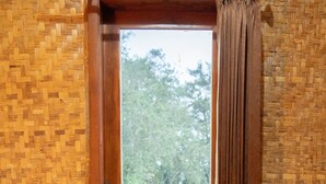 A room with a wooden floor, a window with a view of a pond and greenery, and a curtain on the window. - Villa Situ Patenggang BKSDA (Rancabali)