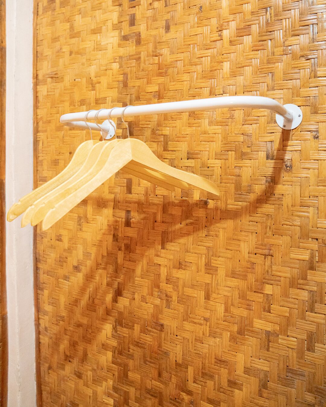 Un mur en bois orné d’un motif tissé, un porte-serviettes blanc avec des cintres jaunes et une serviette blanche.
