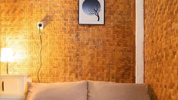 A bedroom with a woven wall, a bedside table with a lamp, and a framed picture of a tree.