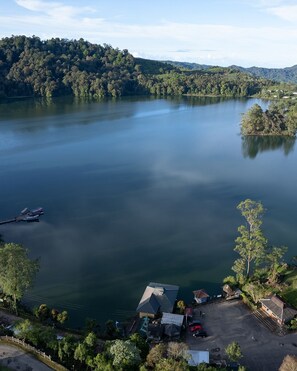 A lakeside property with a dock, a parking area, and a small building with a sloped roof. - Villa Situ Patenggang BKSDA (Rancabali)