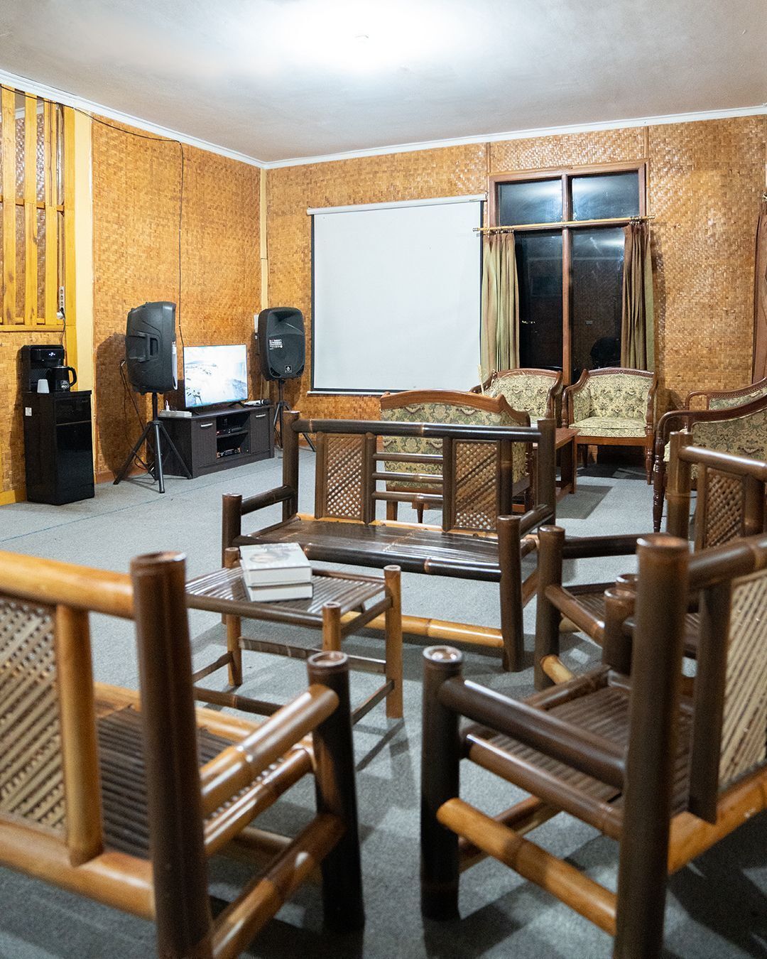 A room with a wooden wall, a whiteboard, a television, speakers, and a seating area with wooden chairs and a sofa.