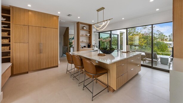 Una cocina moderna con una isla grande, armarios de madera y vistas al exterior.