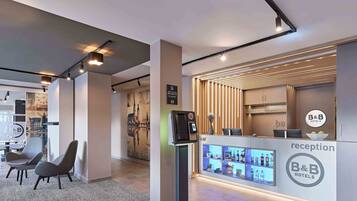 Ein moderner Empfangsbereich mit einer Rezeption, einem Self-Check-in-Terminal und einer Bar.