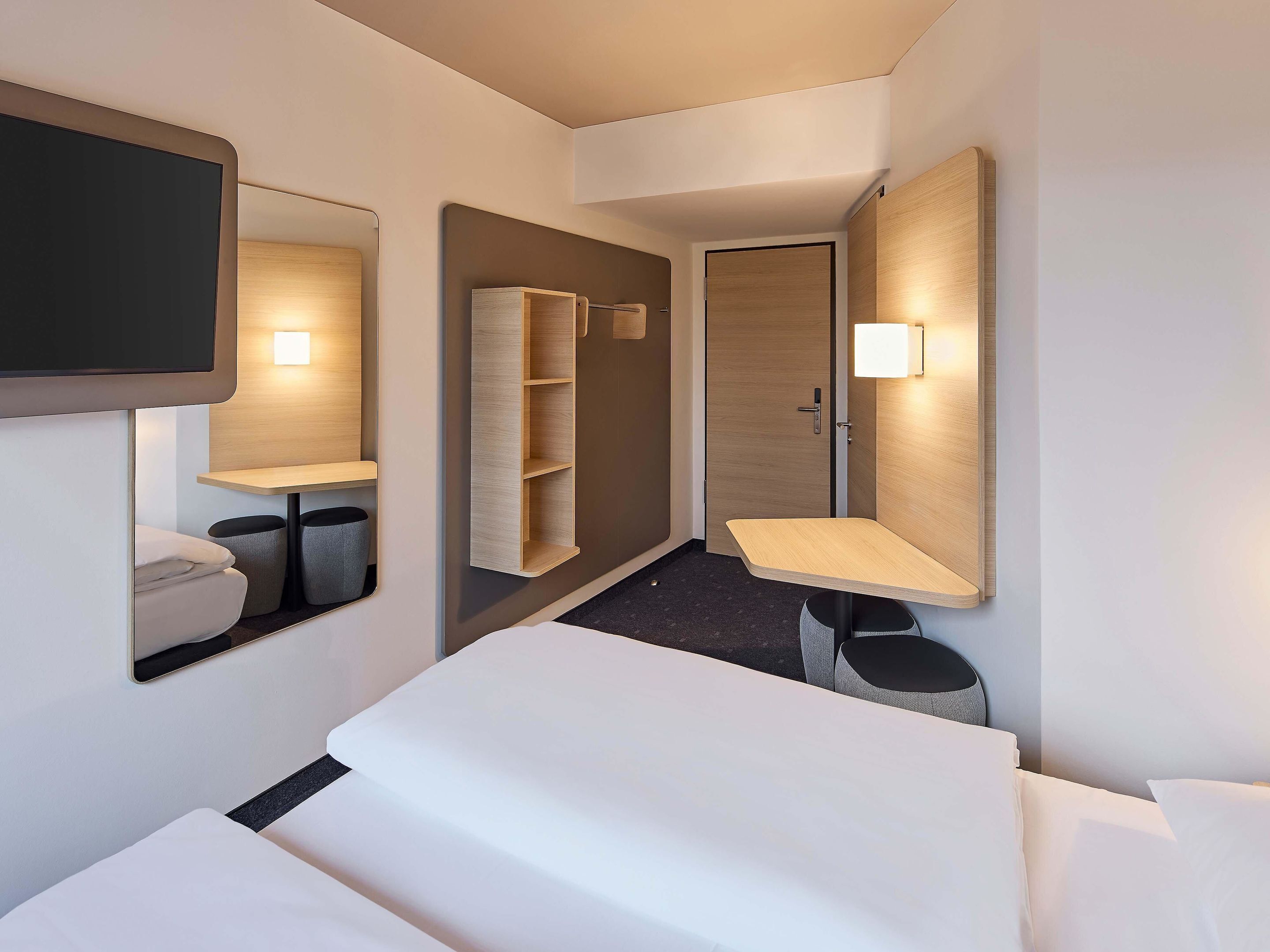 Ein modernes Hotelzimmer mit einem Bett, einem Schreibtisch, einem Spiegel, einem Kleiderschrank und einer kleinen Sitzecke.