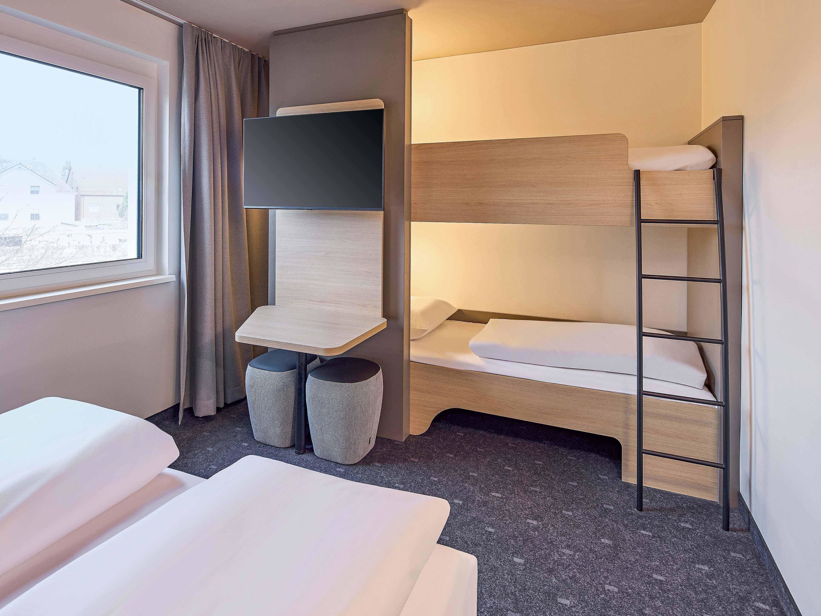Habitación de hotel con literas, un escritorio pequeño y una silla, y una ventana con cortinas.