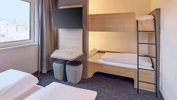 Habitación de hotel con literas, un escritorio pequeño y una silla, y una ventana con cortinas.