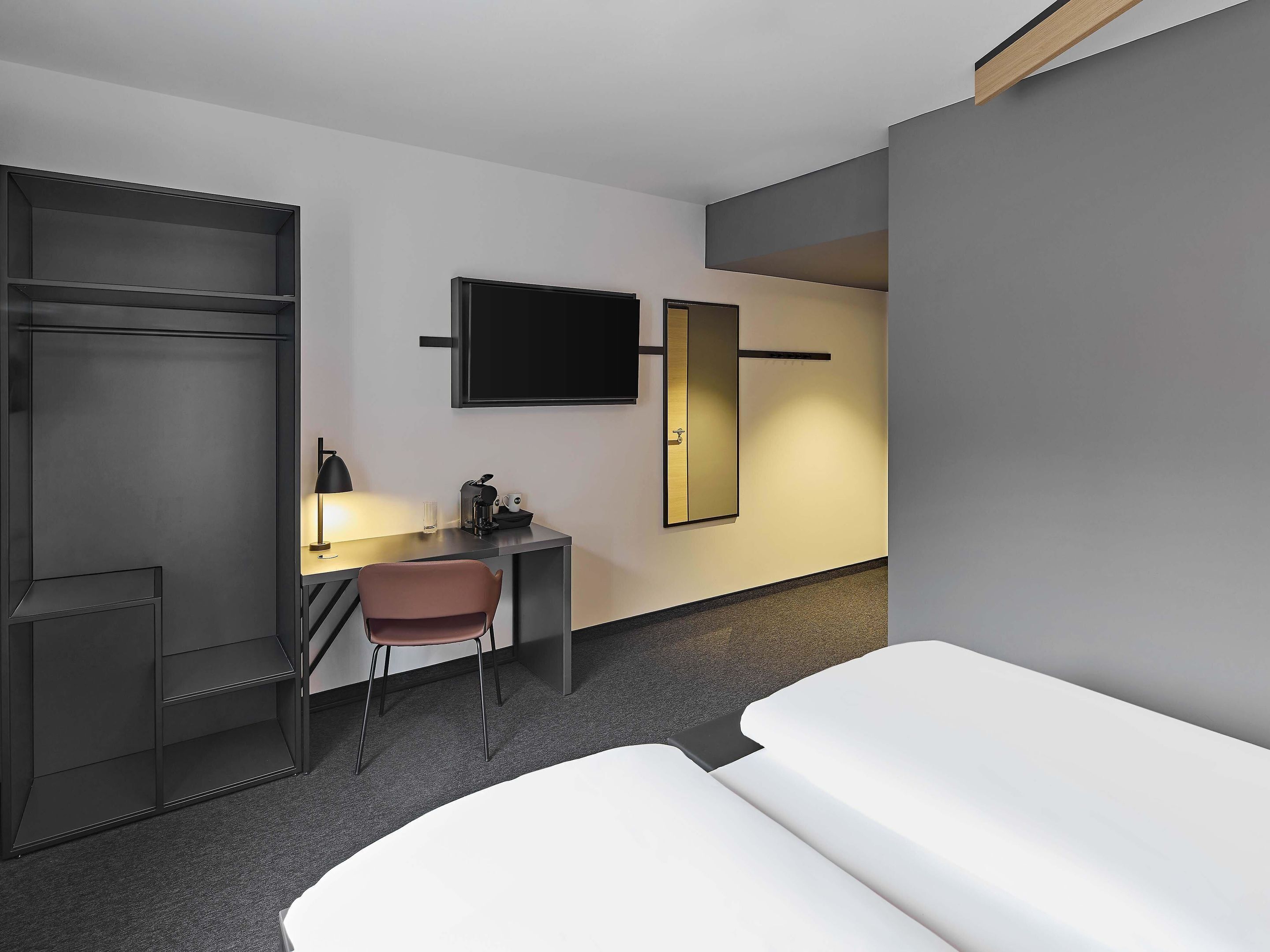 A hotel room with a bed, a desk with a chair, a television, and a wardrobe.