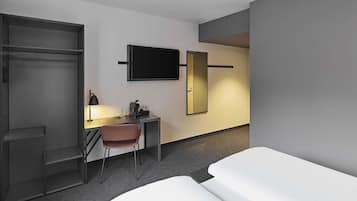 Una habitación de hotel con una cama, un escritorio con una silla, un televisor y un armario.
