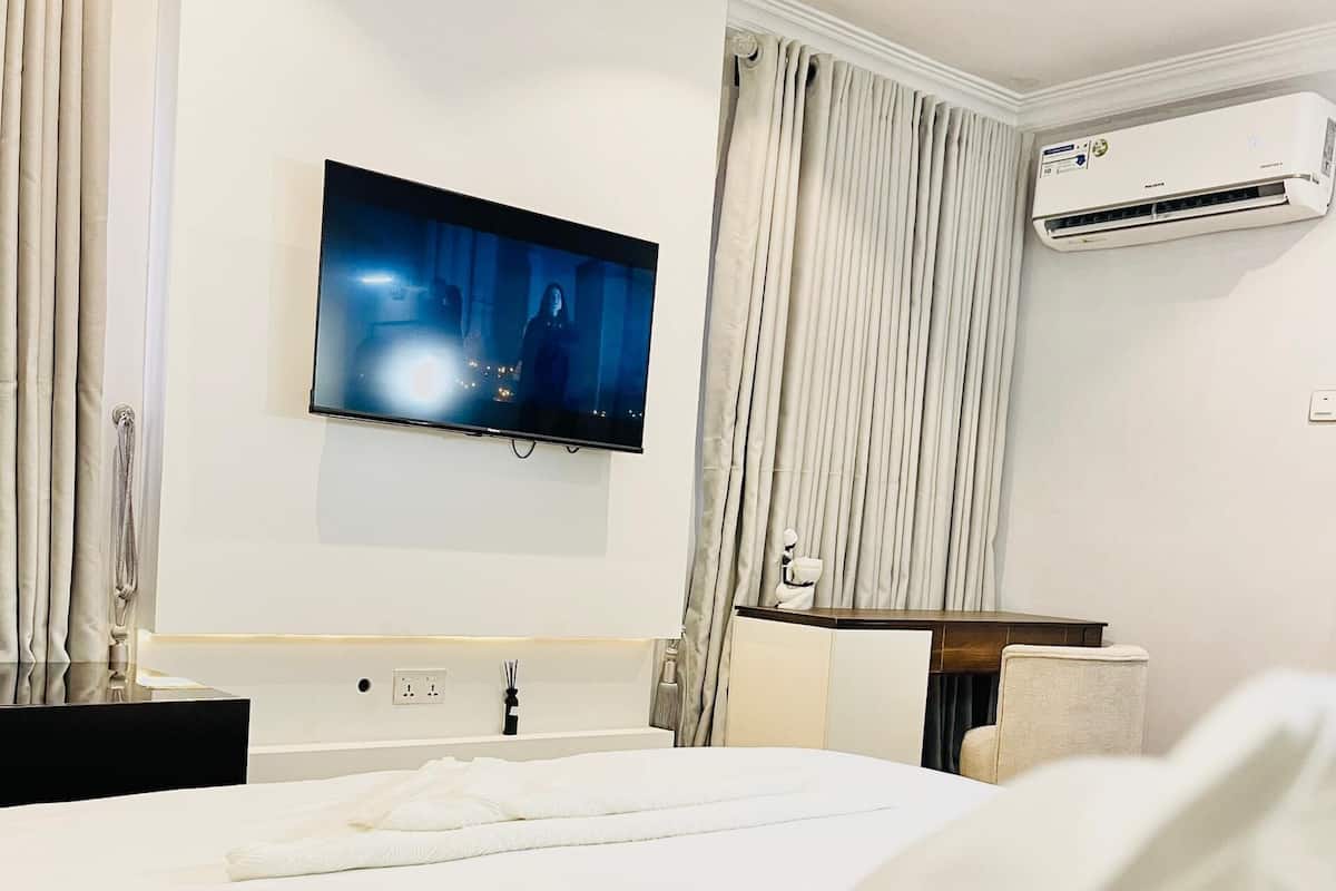 Egy modern szállodai szoba, amelyben egy nagy ágy, egy falra szerelt, síkképernyős televízió, légkondicionáló és egy íróasztal székkkel található.