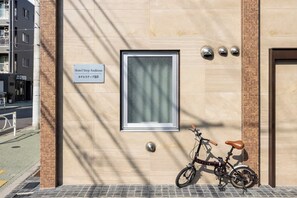 Un edificio con un letrero que indica Hotel Step Asakusa, una bicicleta estacionada afuera y una ventana con una reja de metal.