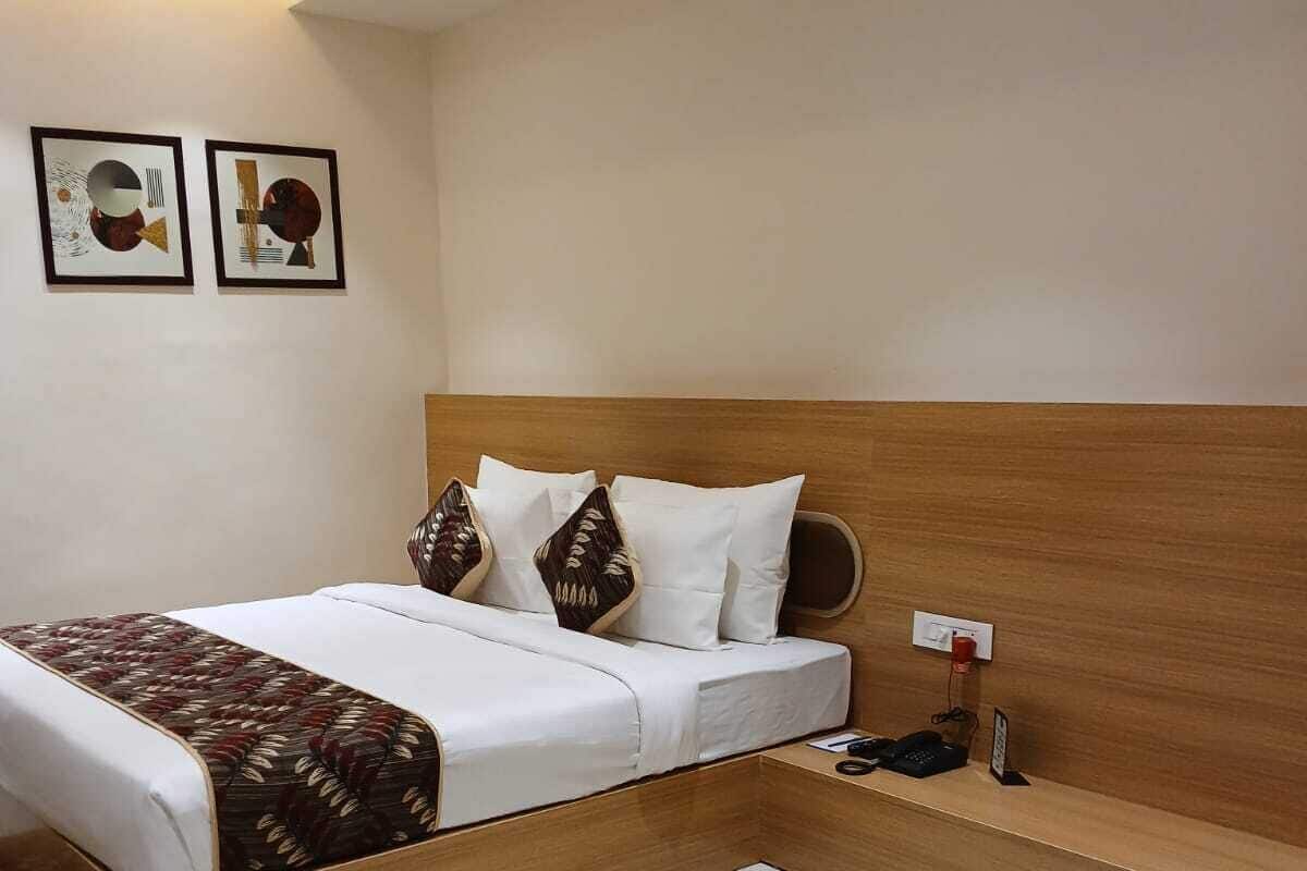 A modern hotel room with a wooden headboard, a neatly made bed with patterned bedding, a bedside table with a phone, and a round wooden table in the center.