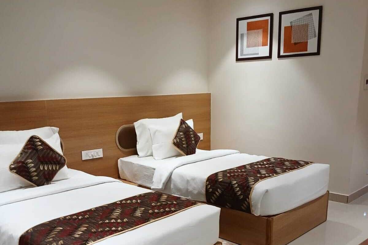 A hotel room with two beds, a wooden headboard, a round wooden table, and two framed pictures on the wall.