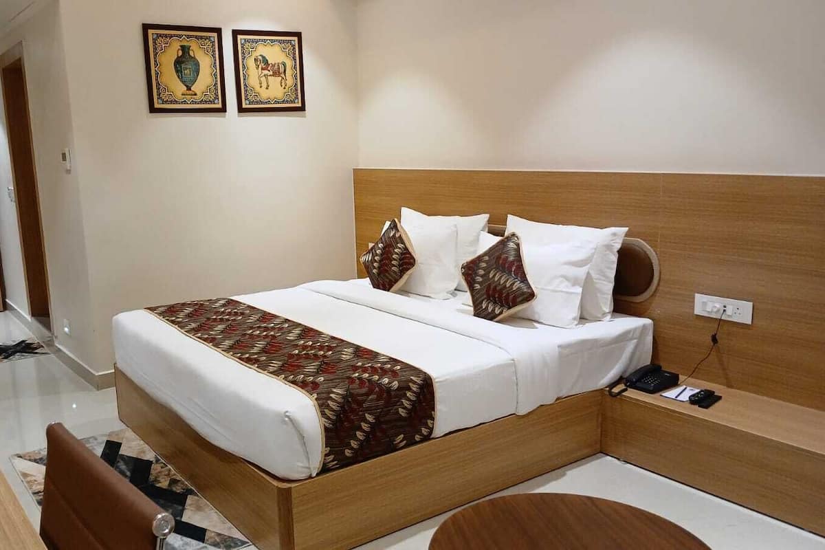 A hotel room with a wooden bed, white bedding, a patterned throw, and two wall-mounted artworks.