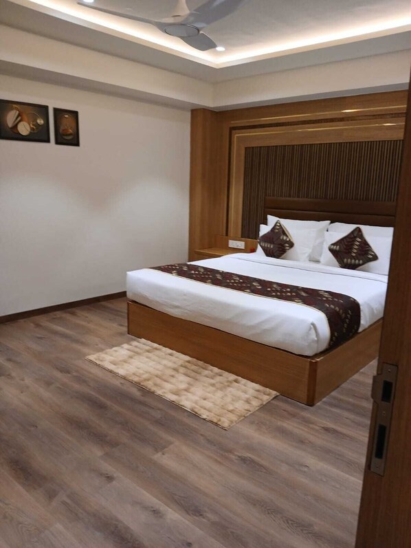 A bedroom with a wooden bed frame, white bedding, and a patterned throw. - The Grand Sita (Jharsuguda)