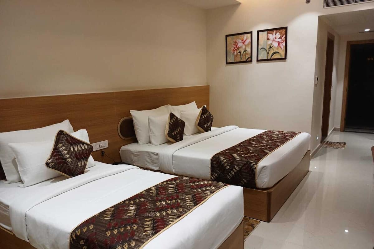 A hotel room with two beds, each with white bedding and decorative pillows. There are two framed floral paintings on the wall.