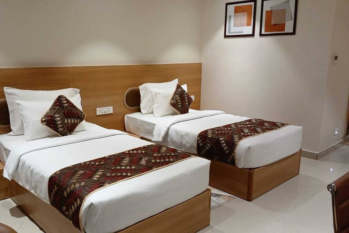 A hotel room with two beds, each with a wooden headboard, white bedding, and patterned throw blankets.