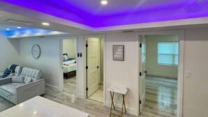 A modern room with a bed, a sofa, a small table, and a door leading to another room. - Wavecrest Retreat (Near Strip & Beach) (Daytona Beach)
