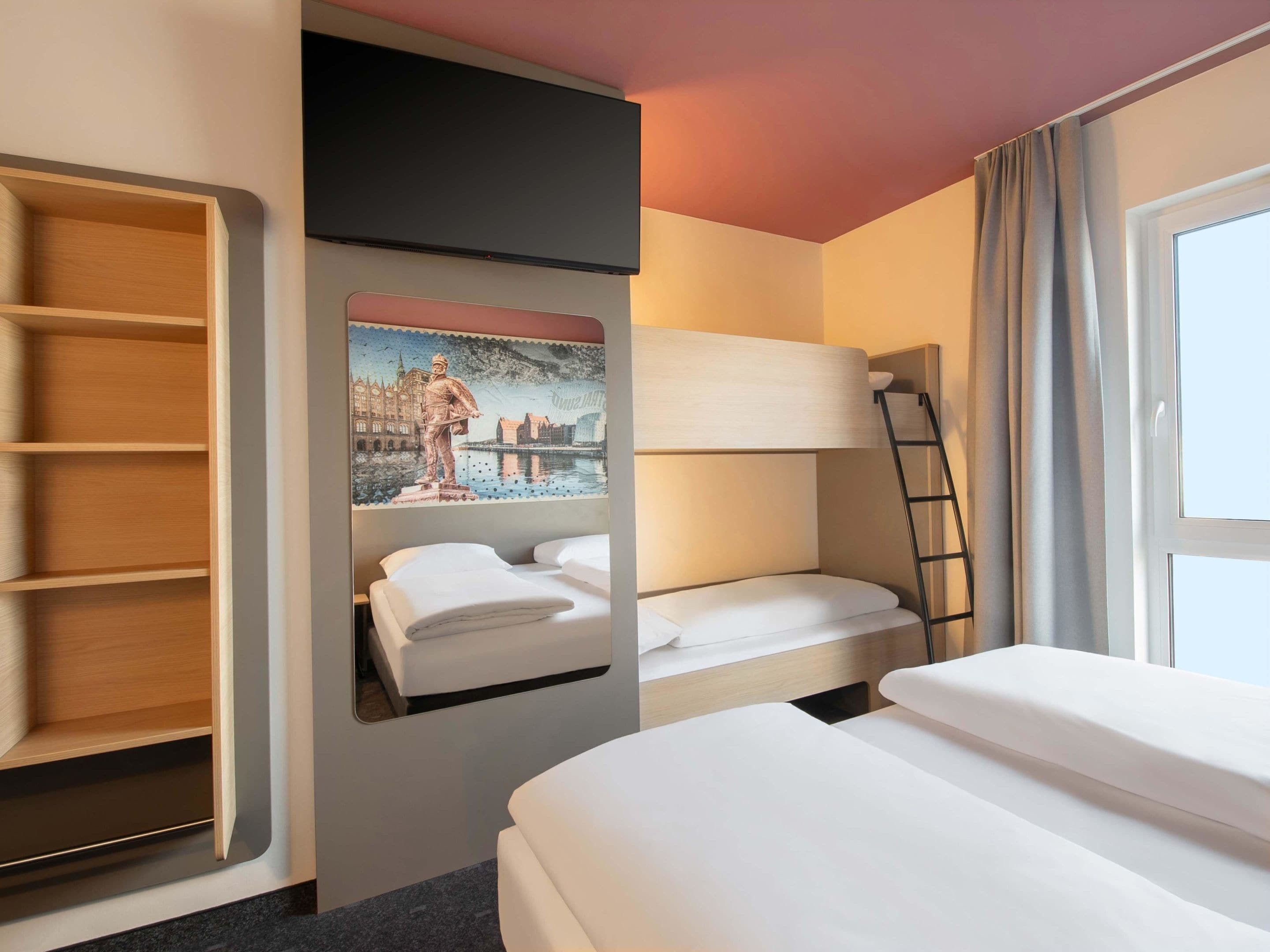 Habitación de hotel con literas, un armario, un cuadro y una ventana con cortinas.