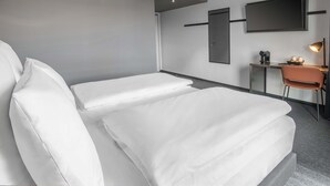 A modern hotel room with a bed, a desk, a chair, a flat-screen TV, and a door. - B&B Hotel Stralsund (Stralsund)