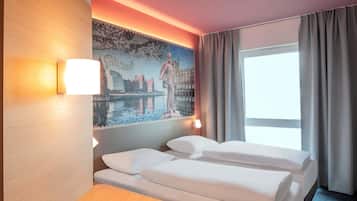 A hotel room with a bed, a desk, a lamp, a painting, and a window with curtains.
