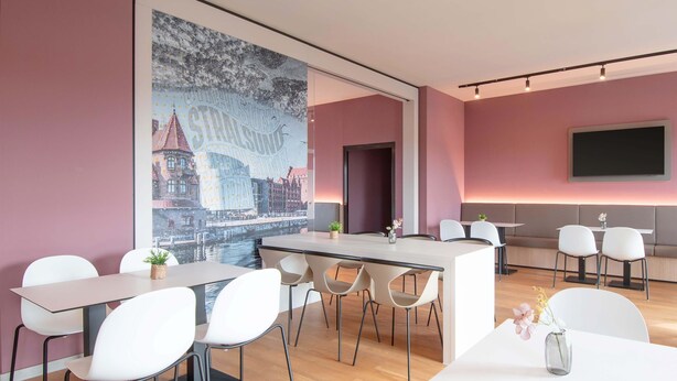 A modern meeting room with a large cityscape mural, a central table, and white chairs. - B&B Hotel Stralsund (Stralsund)