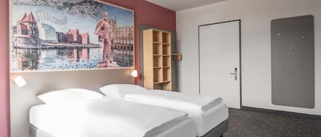 A hotel room with two beds, a large cityscape painting, a wooden shelf, and a door.