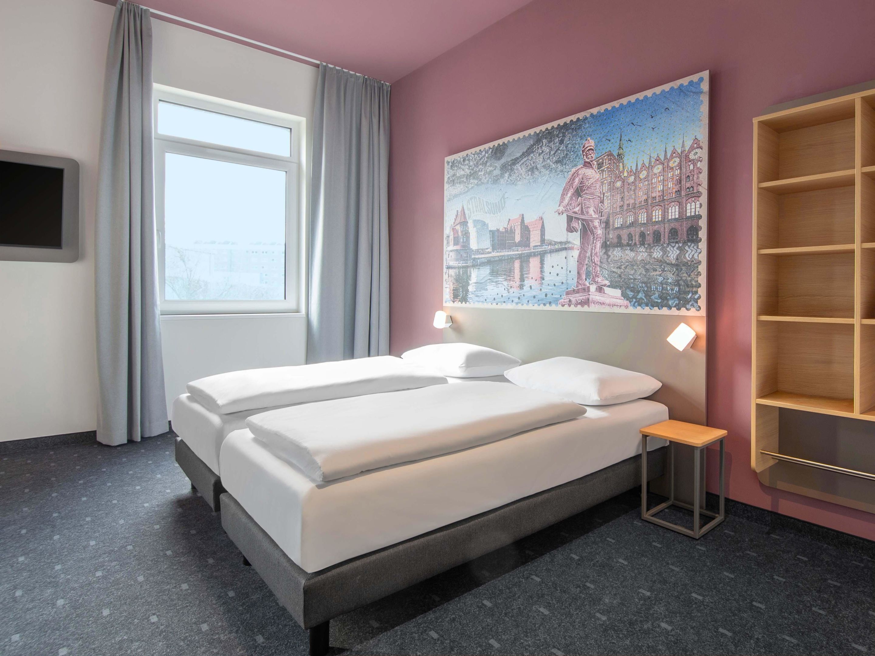 Una habitación de hotel con cama, mesita de noche, un cuadro, ventana y televisión.