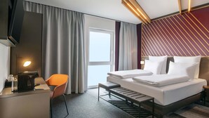 A hotel room with a bed, a desk, a chair, a television, and a window with curtains. - B&B Hotel Stralsund (Stralsund)