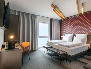 A hotel room with a bed, a desk, a chair, a television, and a window with curtains. - B&B Hotel Stralsund (Stralsund)