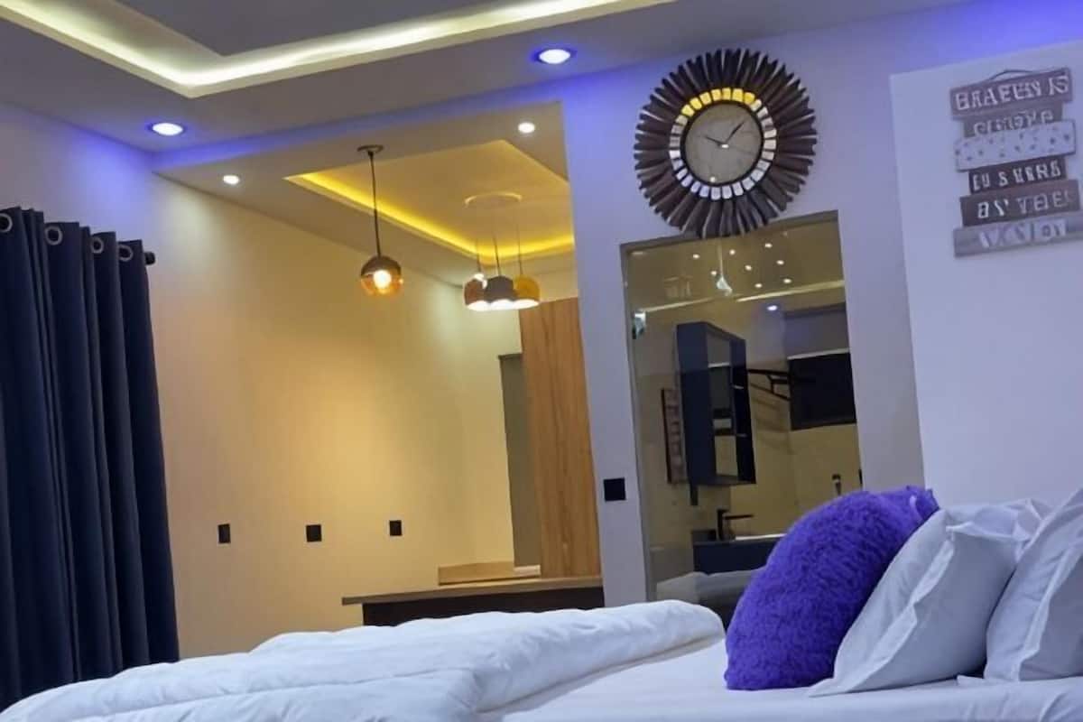 A modern hotel room with a bed, a mirror, a clock, and a wall with a sign.