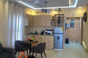 Cocina compacta equipada con refrigerador, microondas y lavaplatos. Comedor con dos sillas y una mesa pequeña.
