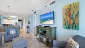 A living room with a television, a sofa, a coffee table, and a painting of seahorses. - Island Royale 403 by Liquid Life (Gulf Shores)
