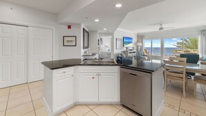 Una cucina moderna con mobili bianchi, lavastoviglie e zona pranzo con vista mare.