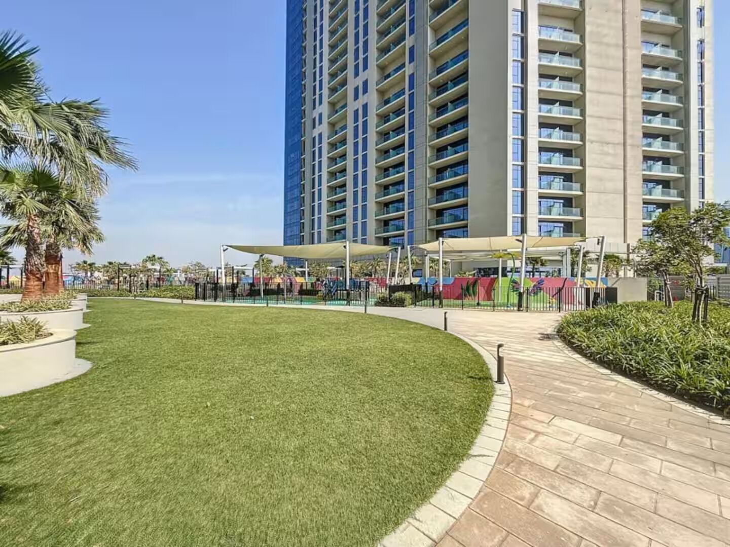 A modern hotel with a central courtyard, a tall building in the background, and a well-maintained lawn.
