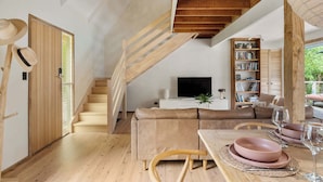 Ein modernes Interieur mit einer Holztreppe, einem Sofa, einem Esstisch mit rosafarbenen Tellern und einem Bücherregal.