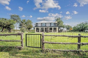 A two-story house with a balcony, surrounded by a wooden fence and a grassy field.